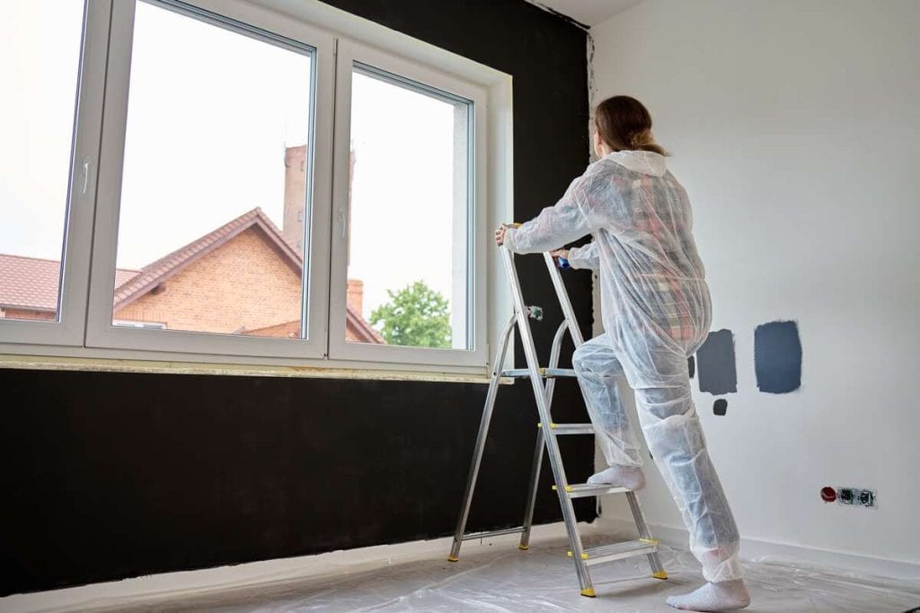 Žmogus dažo kambario sieną juoda spalva – tamsūs tonai vizualiai mažina erdvę, todėl mažiems kambariams rekomenduojama naudoti tik vieną akcentinę sieną.