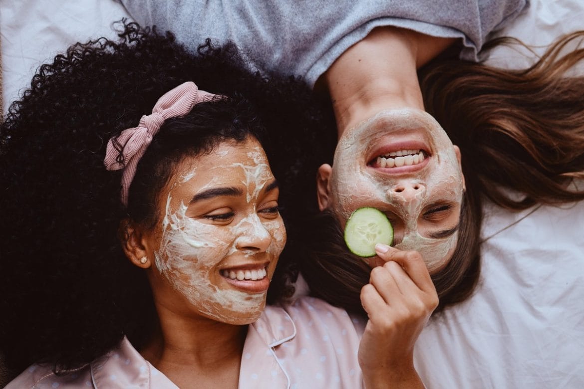 Dvi moterys su veido kaukėmis juokiasi ir atpalaiduoja veido odą.