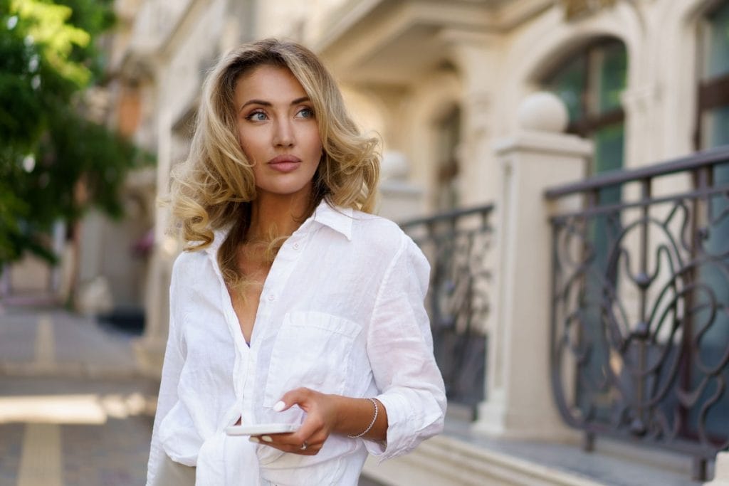 Moteris su baltais marškiniais demonstruoja prancūzių stiliaus paslapčių įkvėptą elegantišką, natūralų įvaizdį.