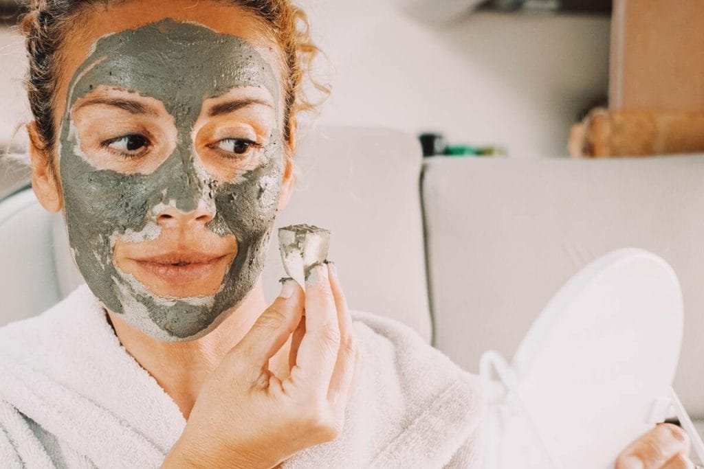 Moteris tepasi veido kaukę iš žalio molio, skirtą riebiai odai prižiūrėti.