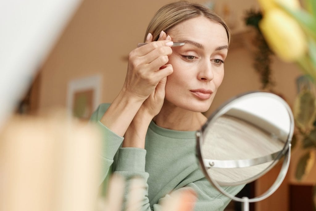 Moteris formuoja antakius pincetu namuose žiūrėdama į veidrodį