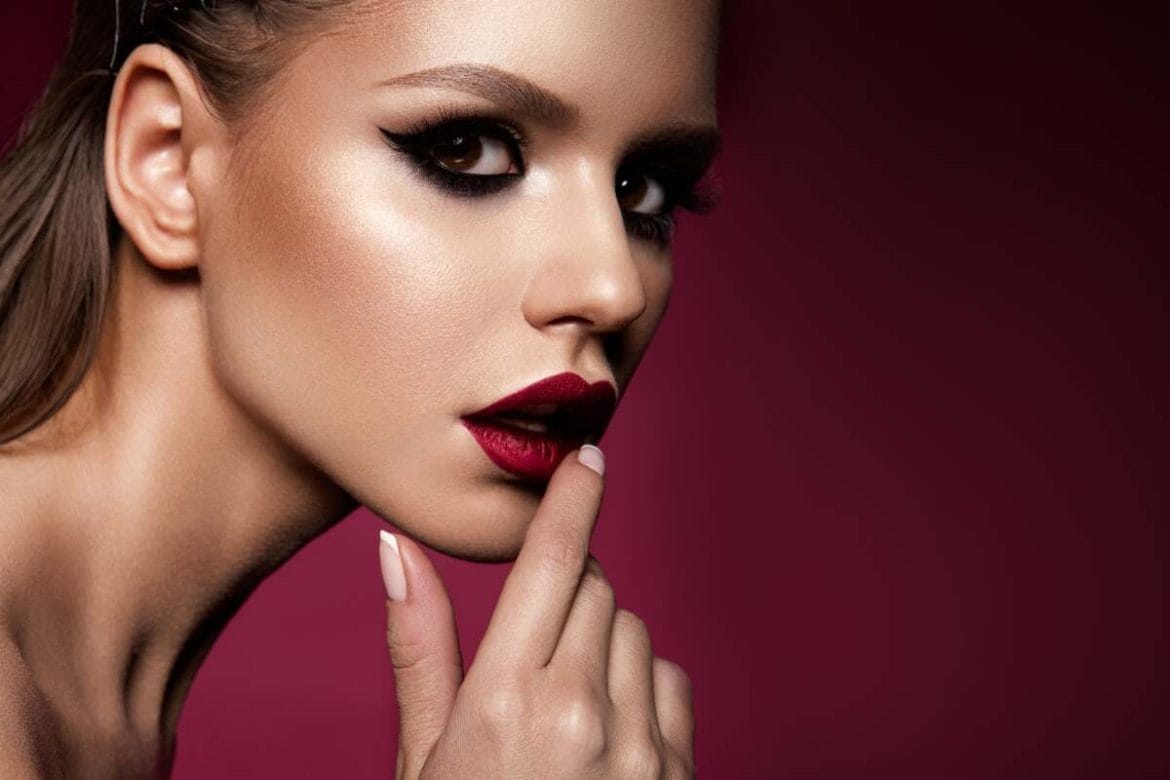 Modelis su išraiškingu dūminiu makiažu, tamsiai paryškintomis akimis ir vakaro įvaizdžiui būdingomis ryškiomis lūpomis.
