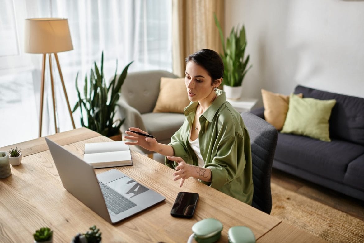Darbas iš namų stilingame biure, moteris kalba per vaizdo skambutį prie darbo stalo svetainėje