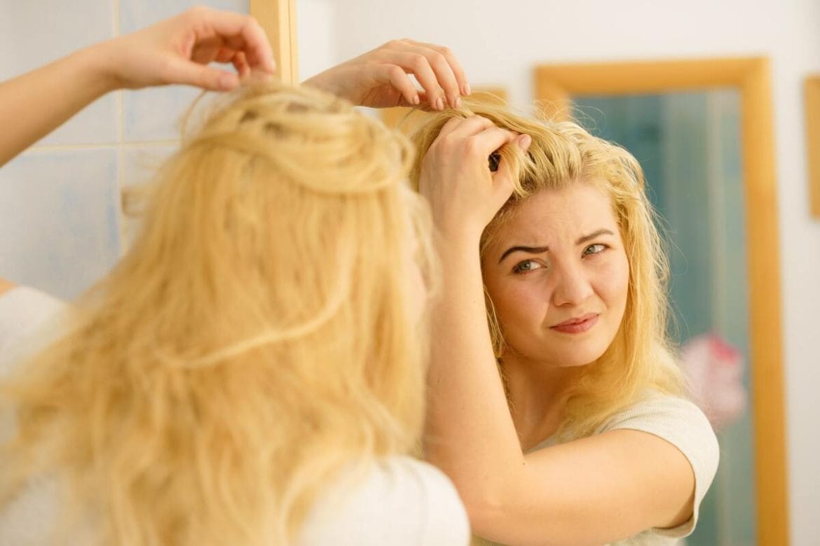 Moteris apžiūri riebaluotus plaukus prie šaknų prieš veidrodį