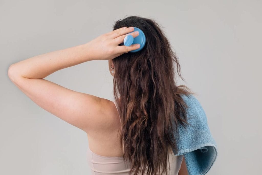 Moteris masažuojasi galvos odą, naudojant rozmarinų aliejaus procedūrą plaukams.