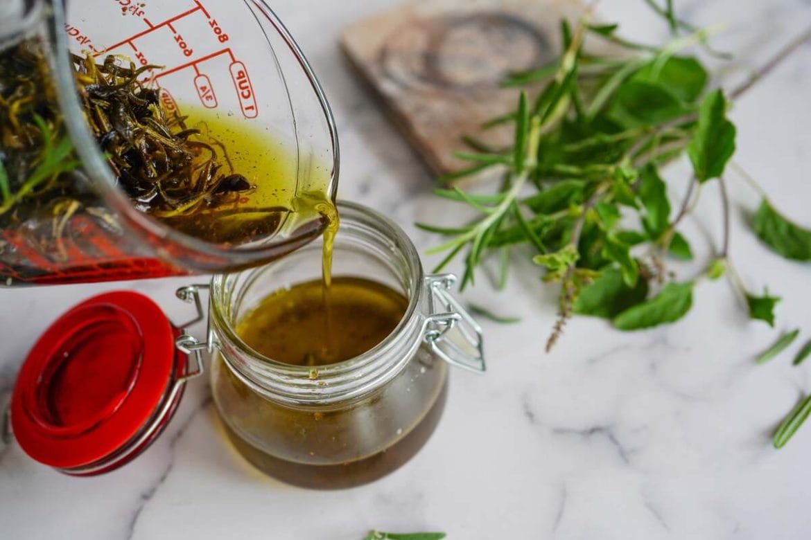 Rozmarinų aliejus plaukams pilamas į stiklainį, šviežios žolelės šalia.