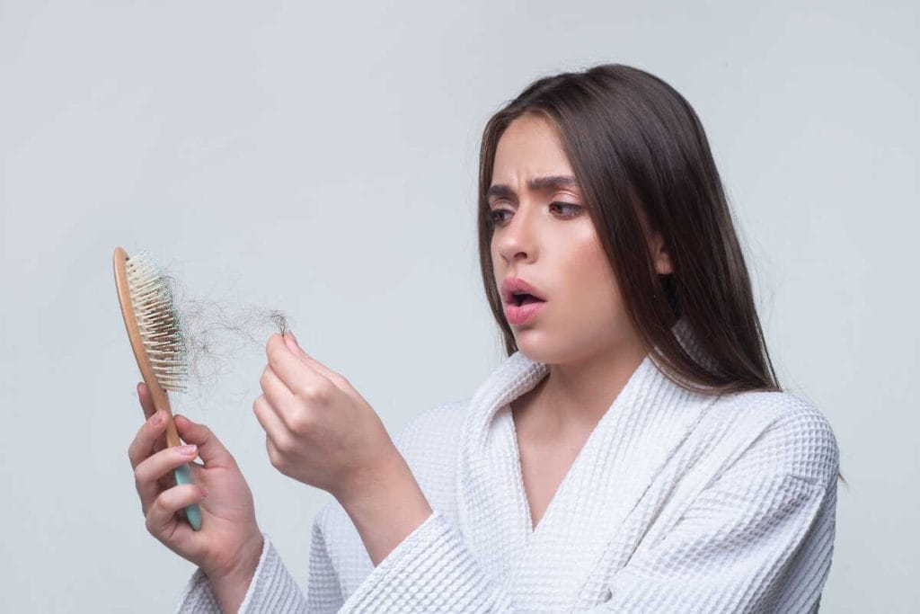 Moteris apžiūri šepetį su iškritusiais plaukais ir pastebi suintensyvėjusį slinkimą