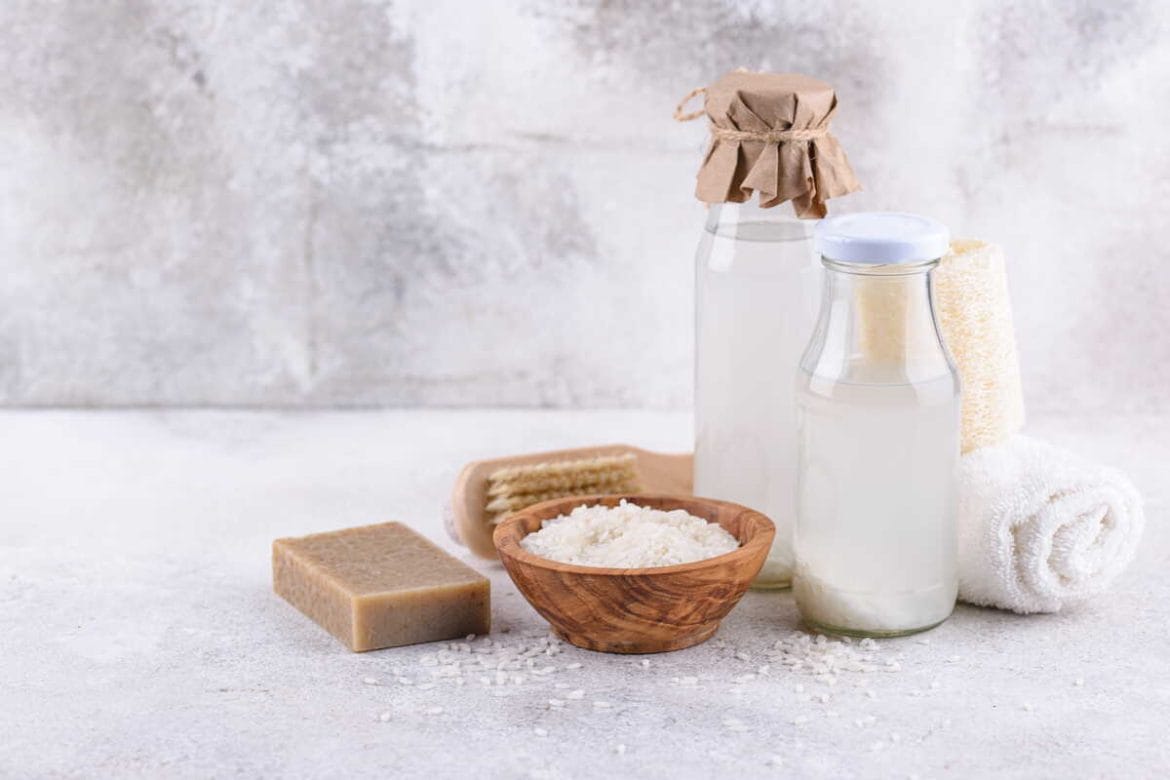 Stikliniai buteliai, kuriuose yra ryžių vanduo plaukams ir dubenėlis su ryžiais