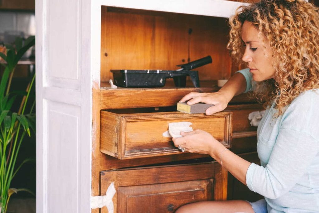 Moteris šlifuoja senos komodos stalčių prieš dažymą