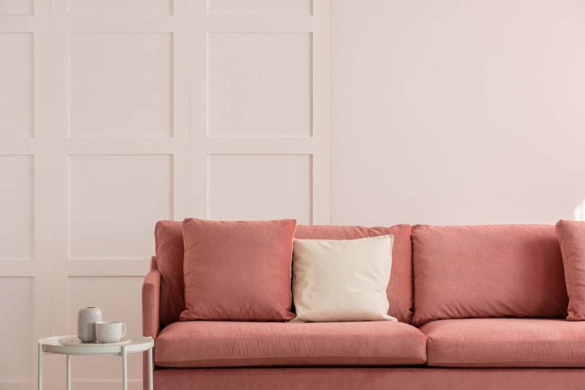 Švelniai rožinė sofa šviesiame kambaryje – pastelinių spalvų pasirinkimas, padedantis vizualiai padidinti mažas erdves.