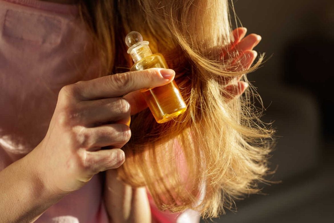 Moteris tepa plaukus aliejumi arba natūraliu skysčiu, laikydama plaukų galiukus rankoje